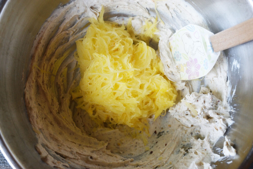 Spaghetti squash fles added to a mixing bowl of cream cheese mix.