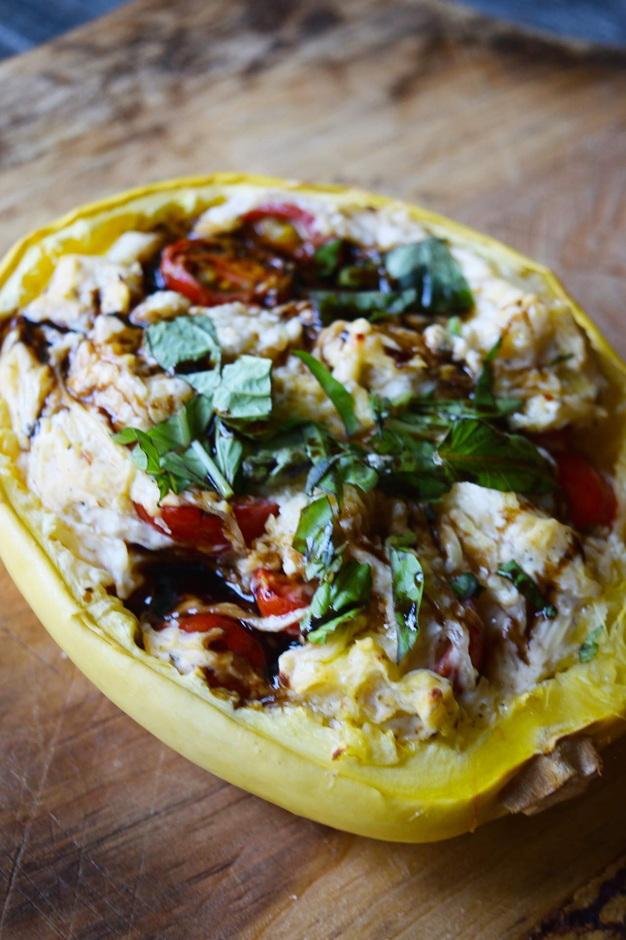 A filled spaghetti squash half sitting garnished on a cutting board.