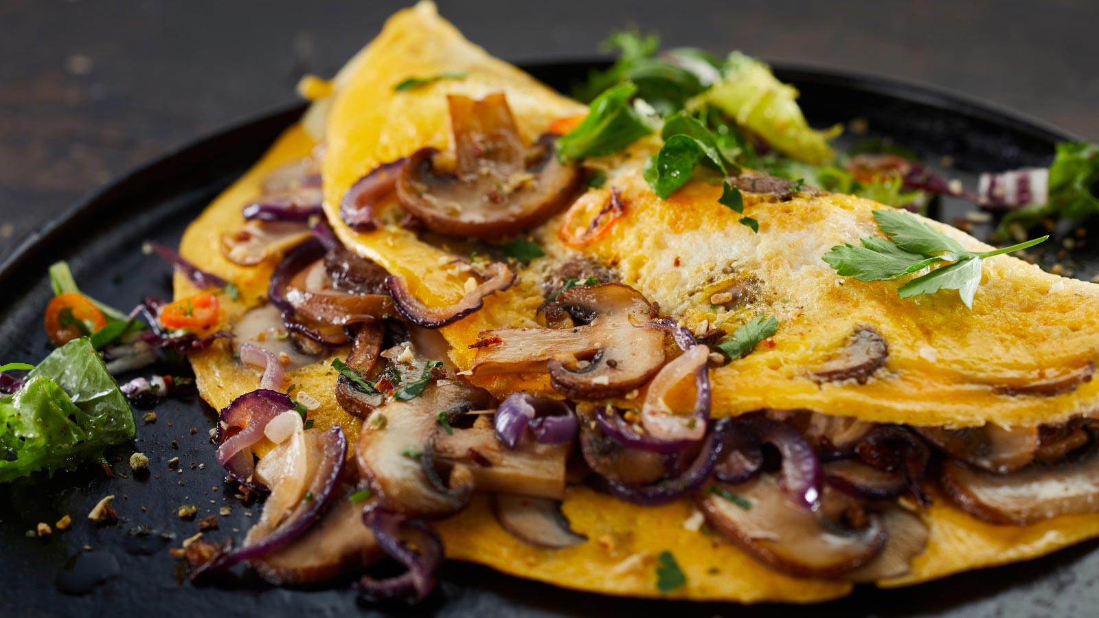 Closeup of delicious omelet with mushrooms and herbs served on a dark platter.