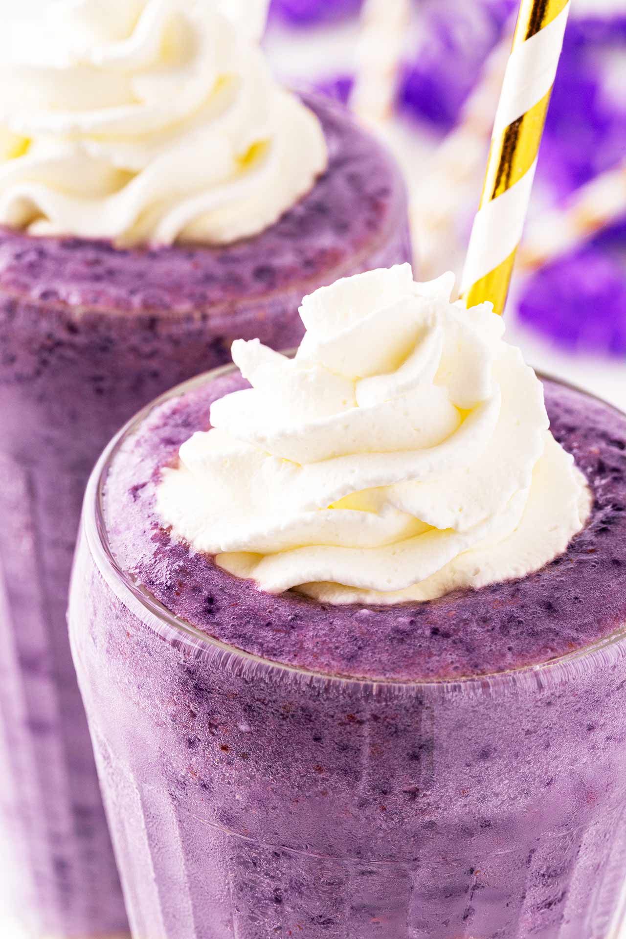 A closeup of two glasses filled with Grimace Shake and topped with dollops of whipped cream.