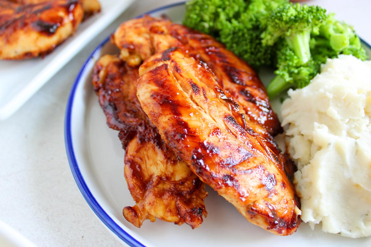 A closeup of chicken tenders on a plate with mashed potatoes and broccholi.