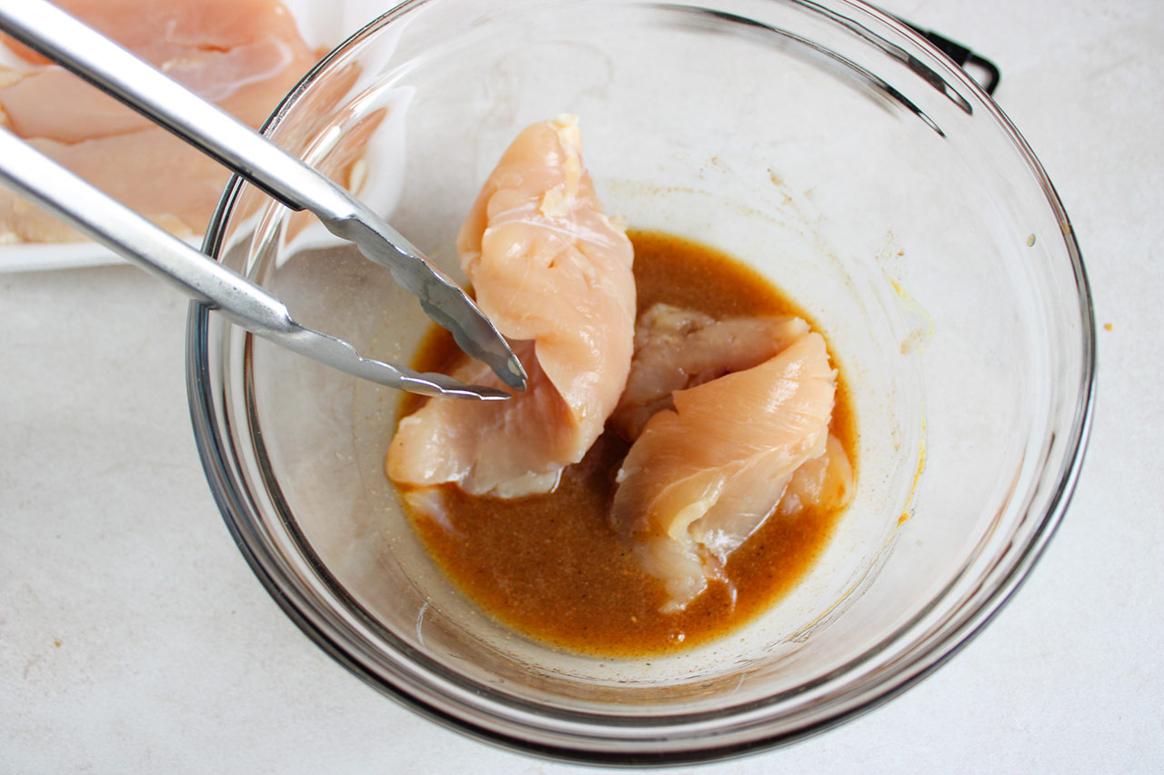 Marinating chicken tenders in marinade in a mixing bowl.