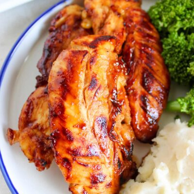 A closeup of honey mustard chicken tenders on a plate with mashed potatoes and broccoli.