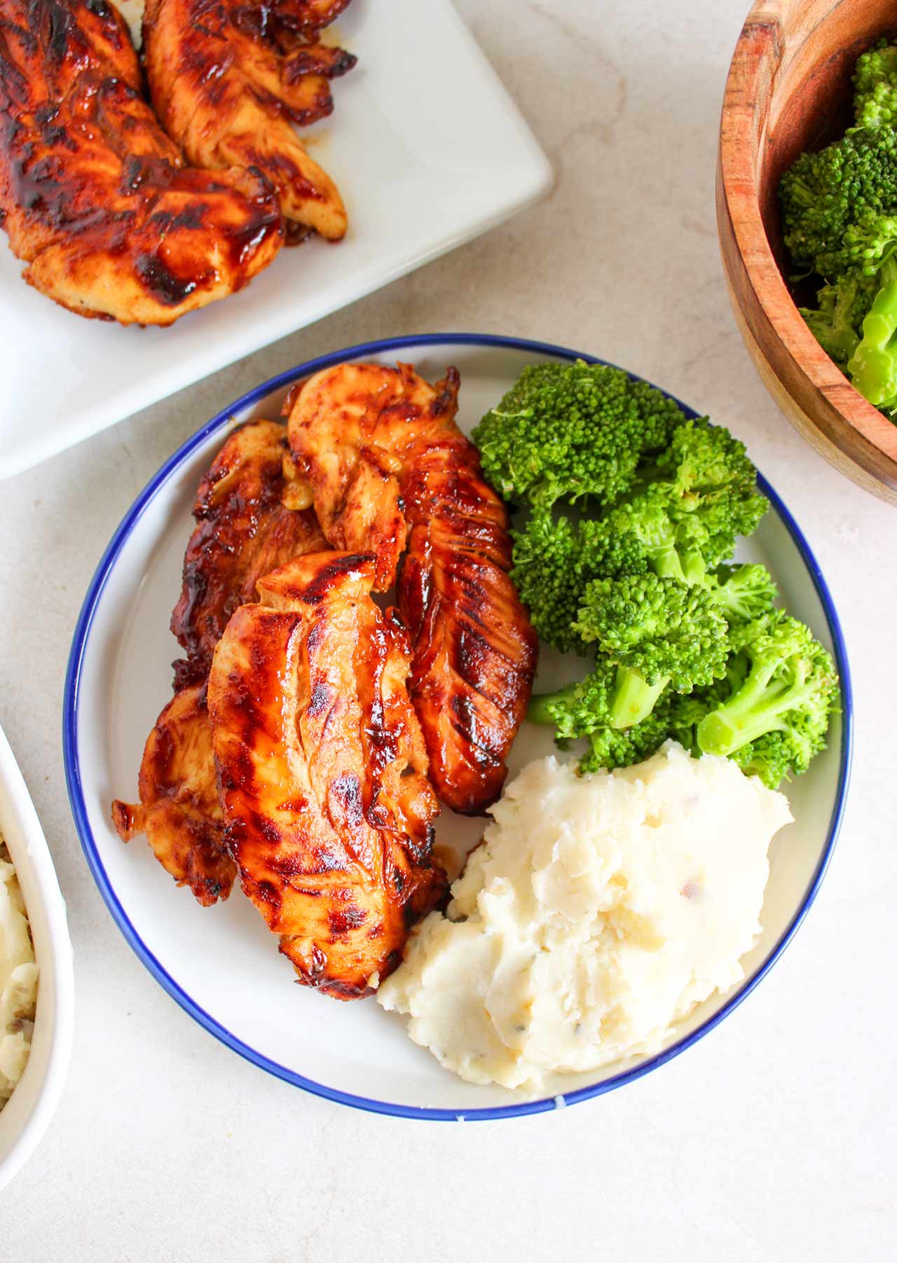 An overhead view of some honey mustard chicken tenders on a plate with broccoli and mashed potatoes.