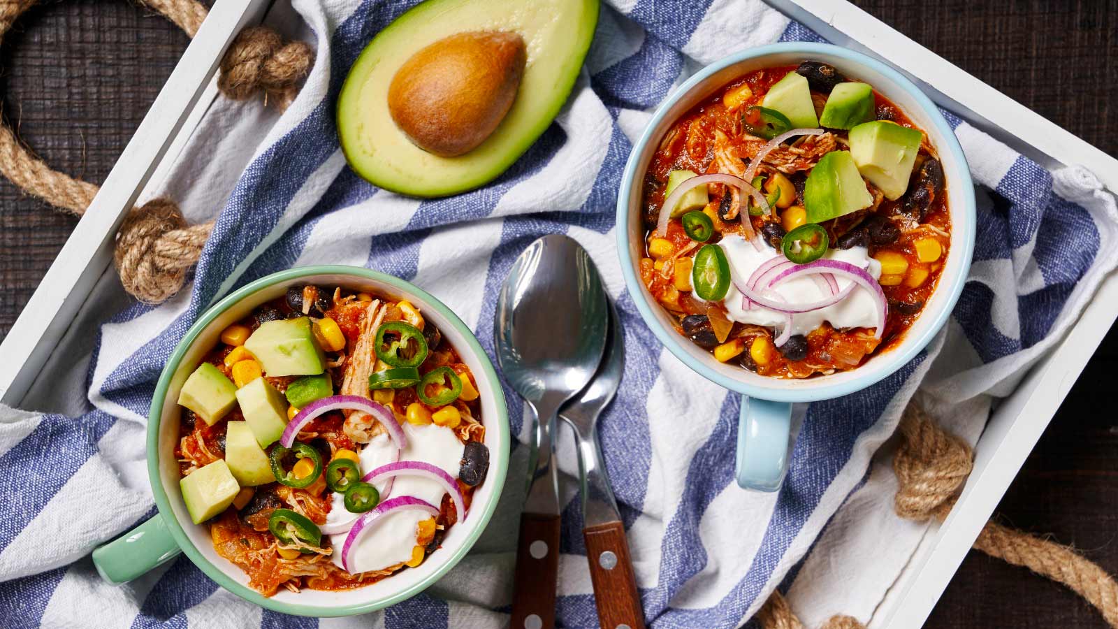 Shredded Mexican chicken and toppings served in mugs with sour cream, avocado, and red onion, on a white tray.