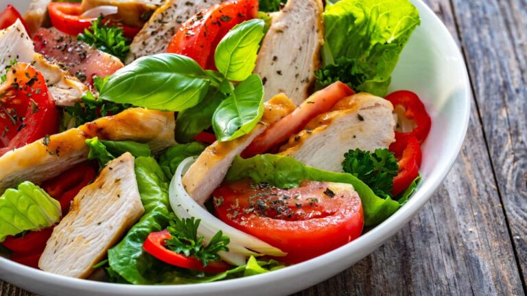 Caesar style salad - grilled chicken breast and fresh vegetables on wooden table.