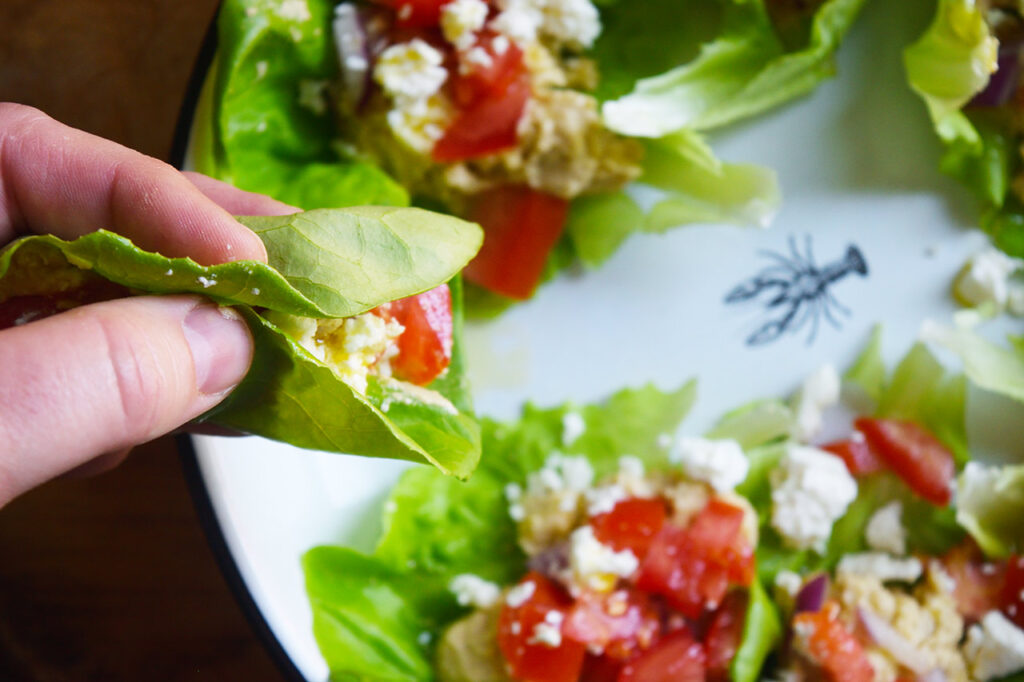 A hand holds a Mediterranean Lettuce Wrap from a platter full of them.