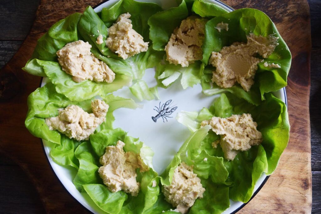 Hummus spooned onto lettuce leaves on a platter.