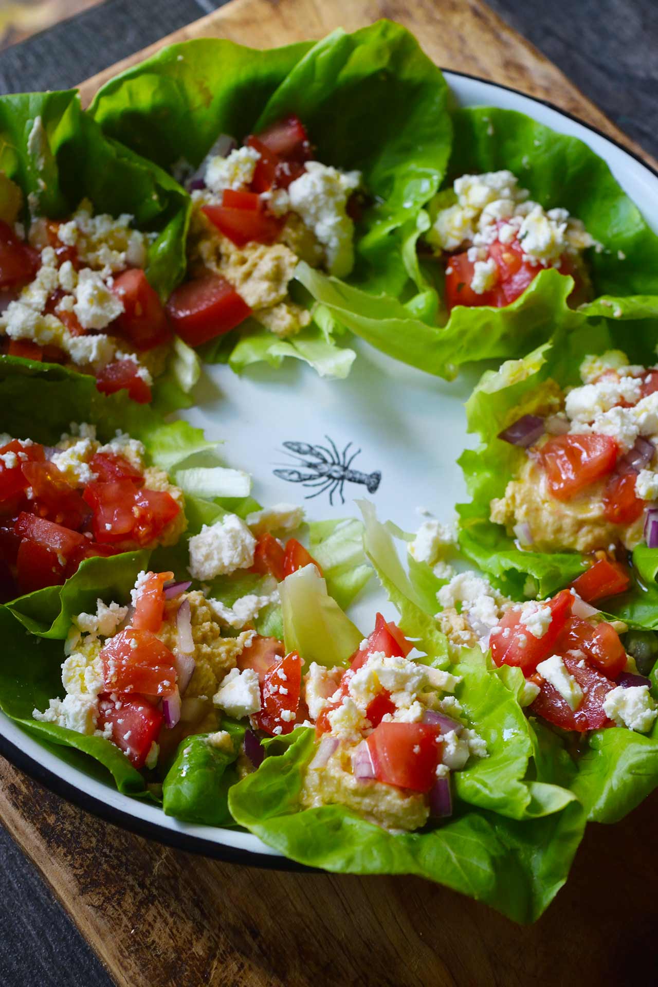 A side angled view of a platter of Mediterranean Lettuce Wraps sitting on a wood cutting board.