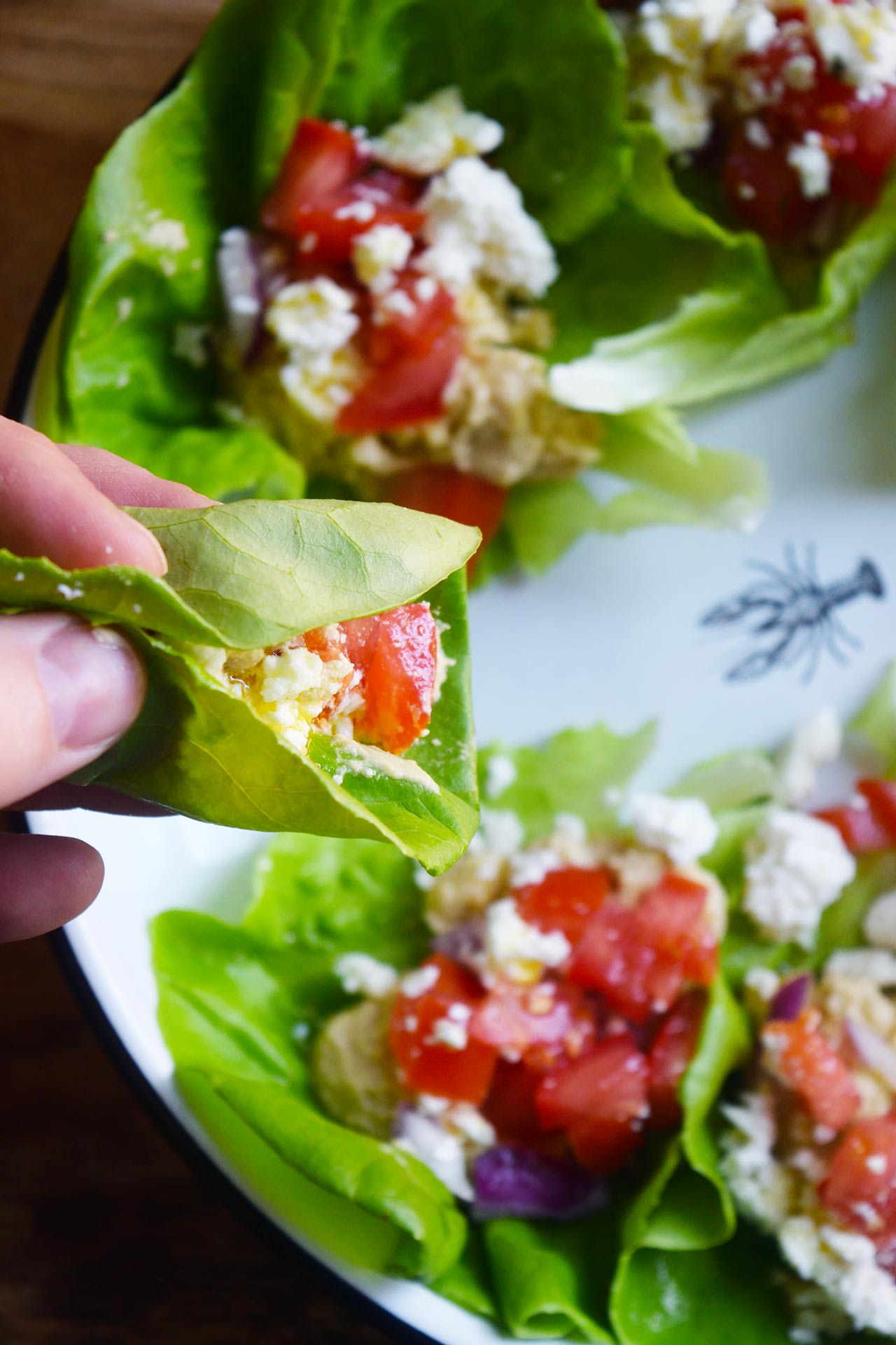 A hand holds up a Mediterranean Lettuce Wrap taken from a platter full.