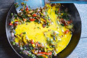 Beaten eggs added to vegetables in a skillet.