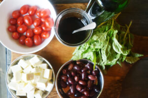 Ingredients for Mediterranean Skewers in individual bowls on a wood cutting board.