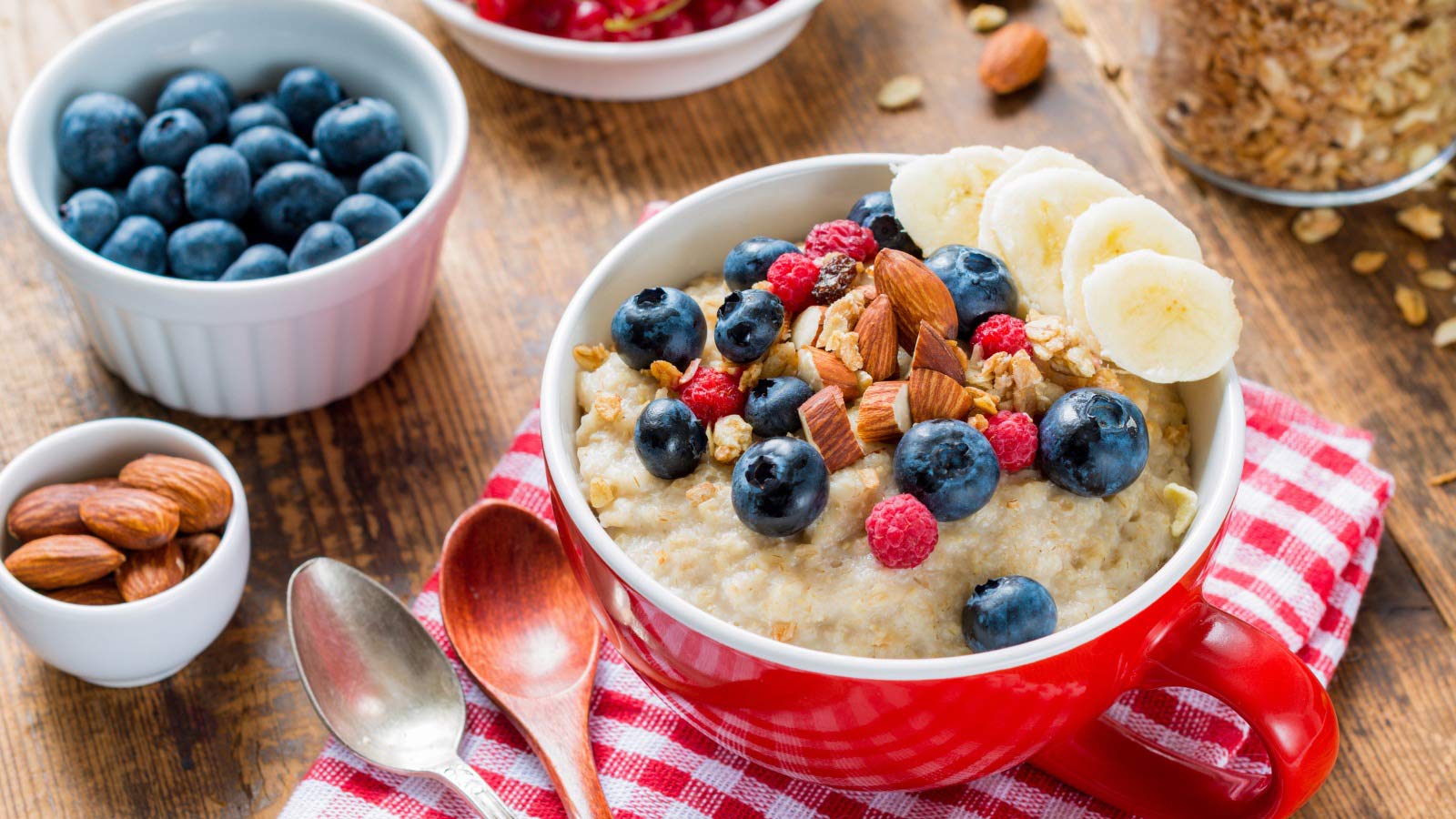 Oatmeal porridge with fresh blueberries, raspberries, muesli and almonds in red bowl. Healthy breakfast, healthy eating, vegan food concept.