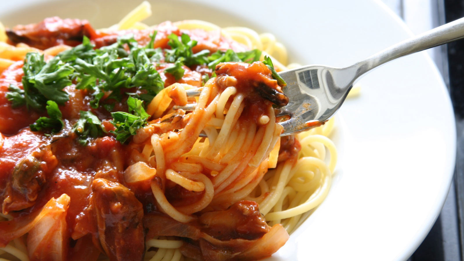 Spaghetti with tomato sauce and parsley garnishing (about to taste it using a fork)