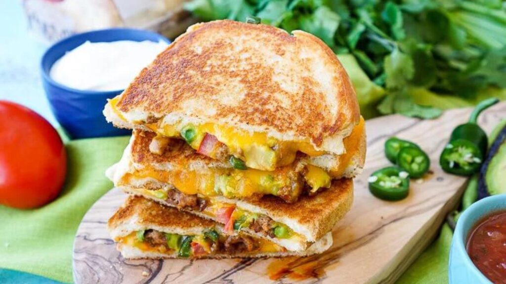 A stacked taco grilled cheese on a cutting board.
