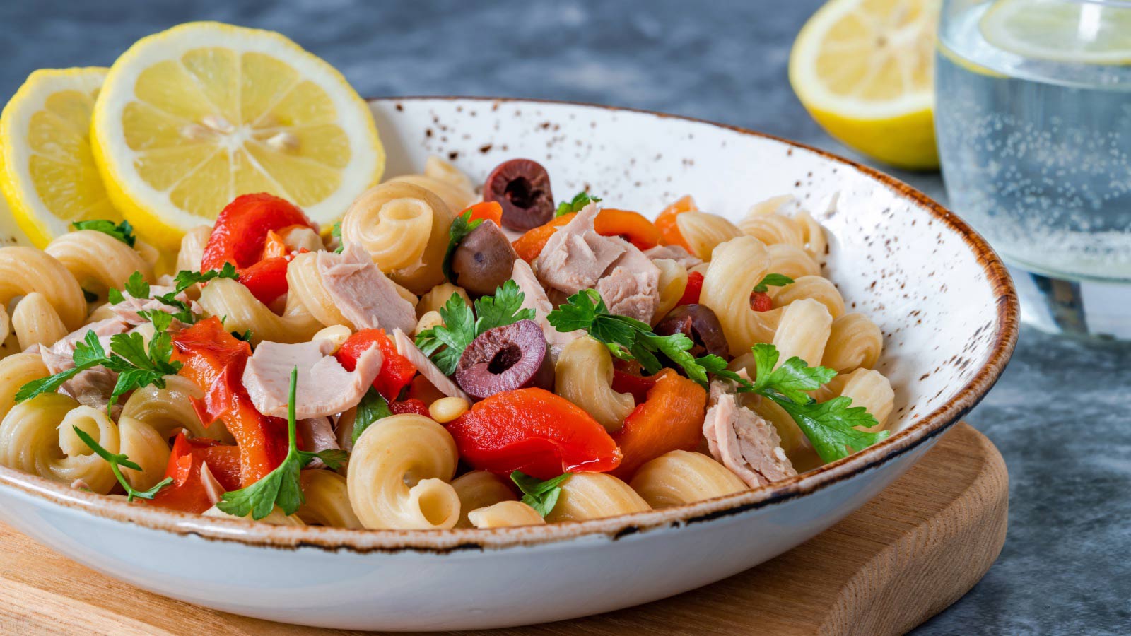 Warm pasta salad with tuna and veggies in a bowl with two lemon slices.
