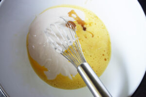 A mixing bowl with whisked eggs, yogurt, and honey.