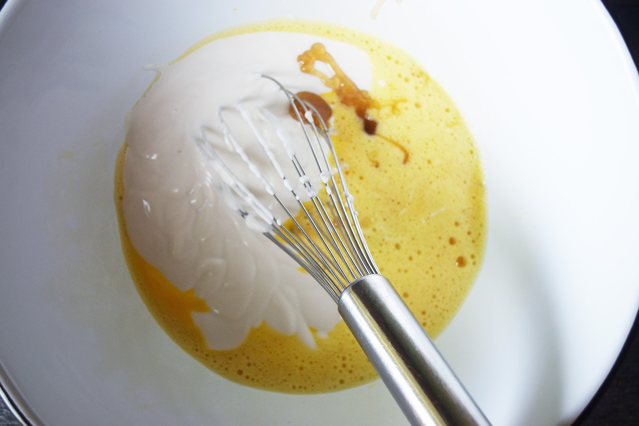A mixing bowl with whisked eggs, yogurt, and honey.