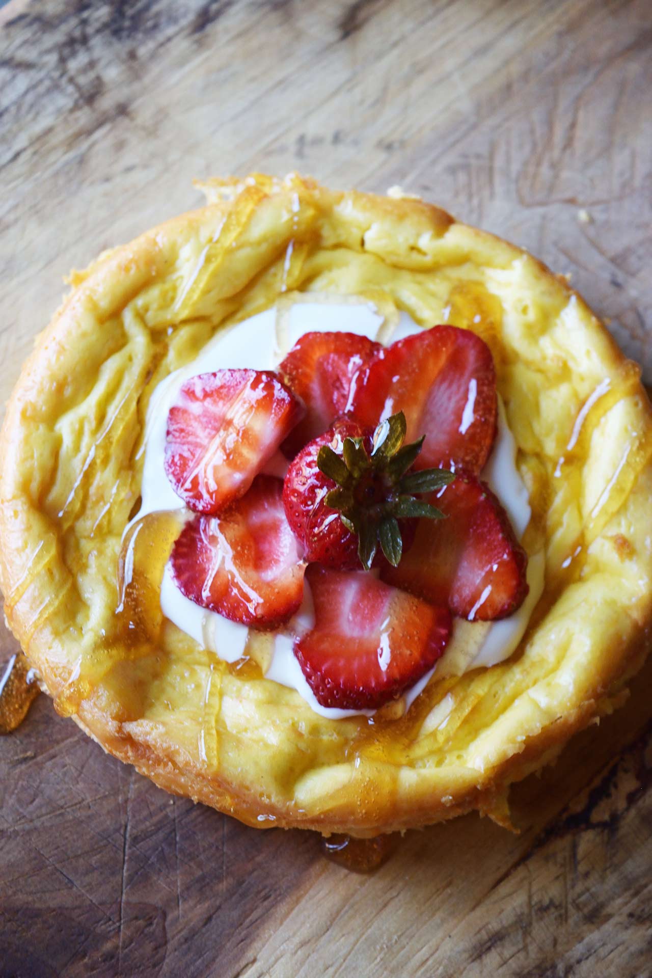 An overhead view of a yogurt cake topped with yogurt, fresh strawberries, and a drizzle of honey.