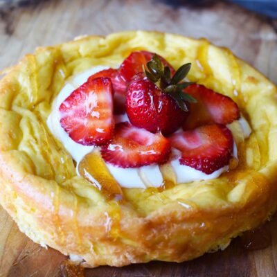A front view of a garnished yogurt cake on a wood cutting board.