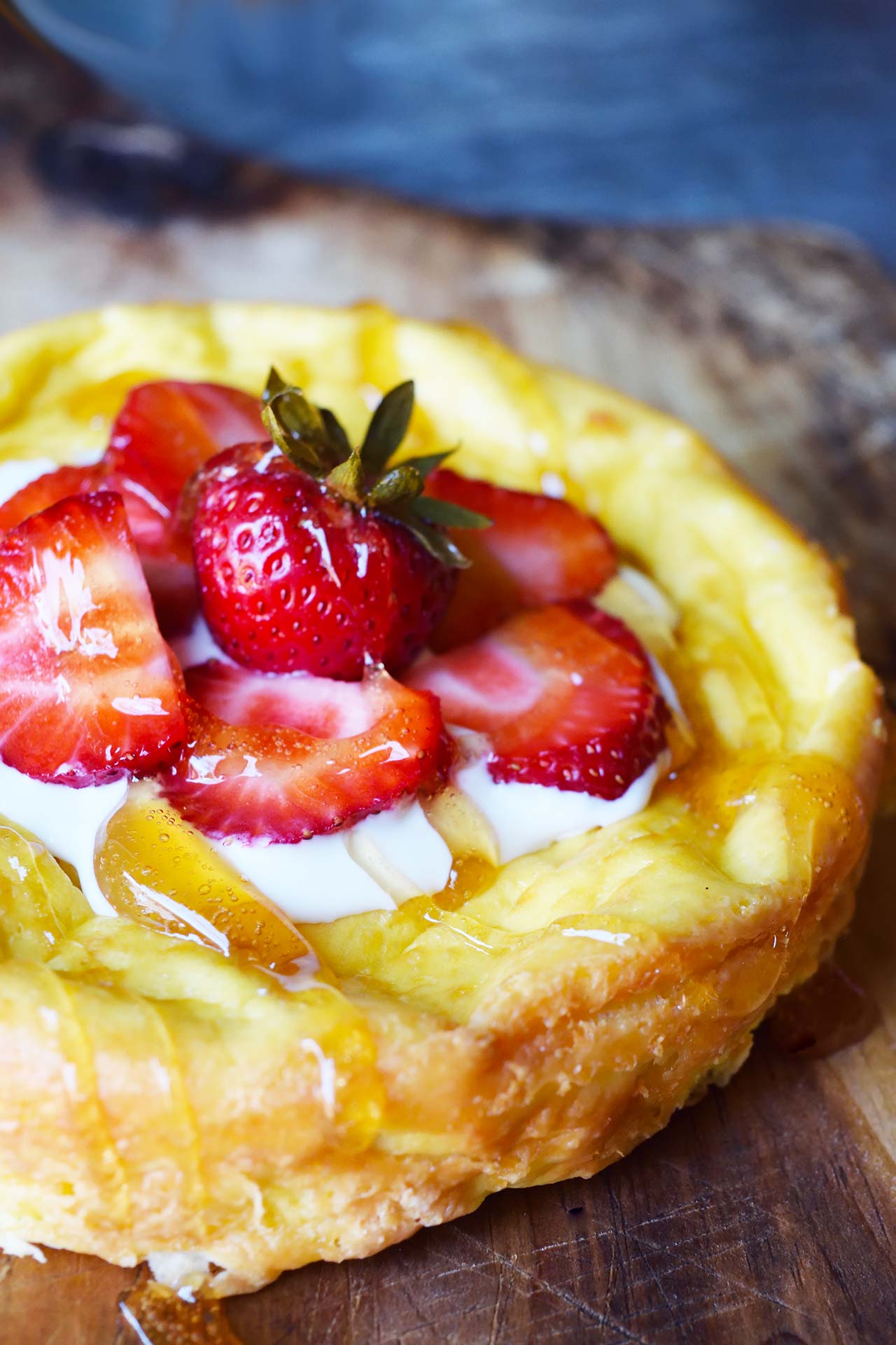 A side view of a yogurt cake sitting on a wood cutting board, topped with fresh strawberries and yogurt.