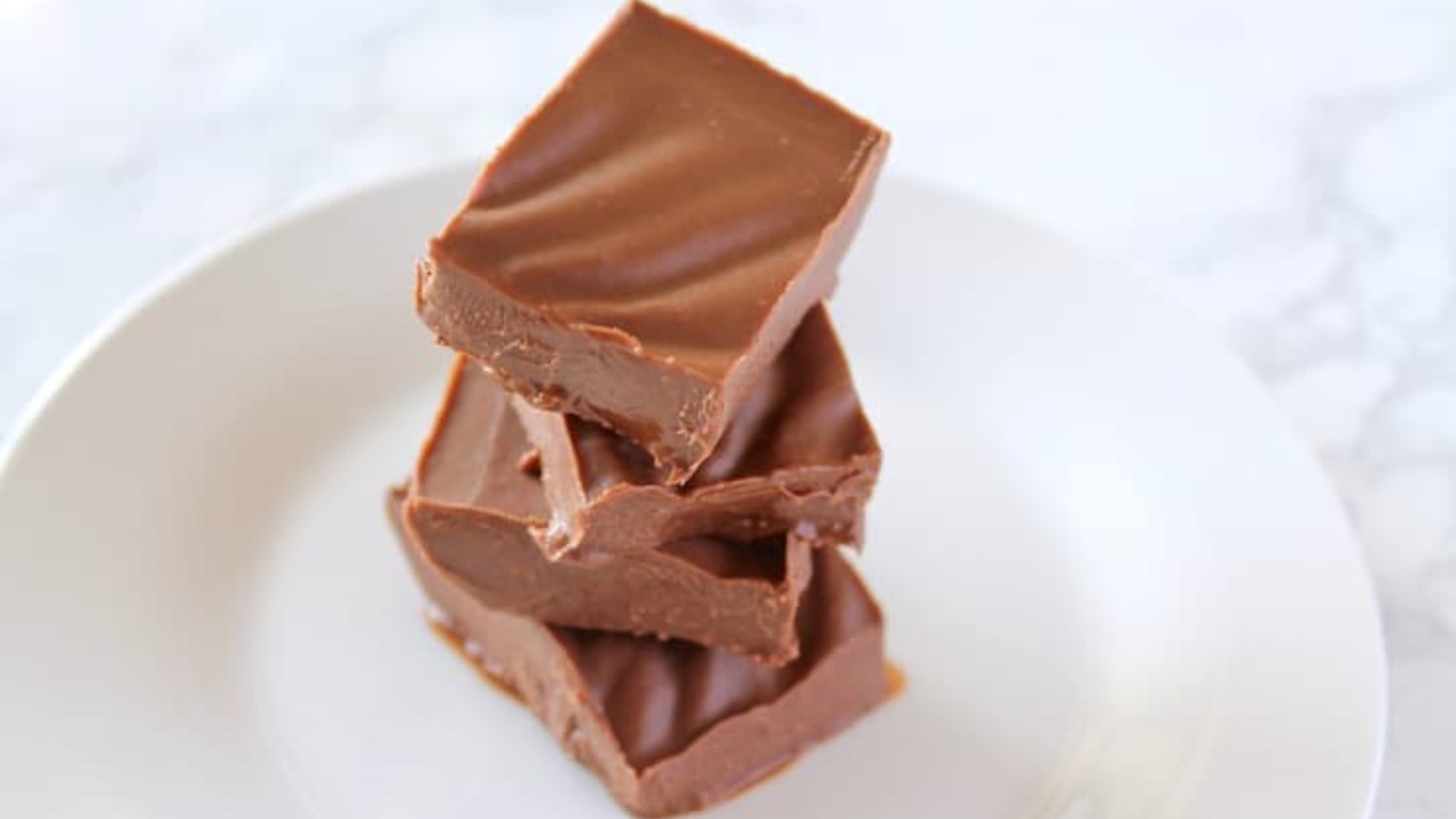 Four pieces of fudge stacked up on a white plate.