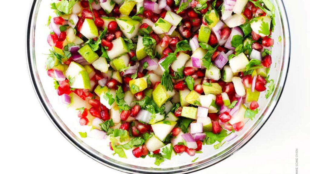 An overhead view of Pear Pomegranate Salsa in a glass bowl on a white background.