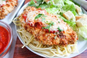 Side view of a breast of Air Fryer Chicken Parmesan on a bed of spaghetti noodles on a white plate.