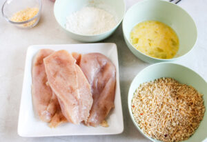 Seasoned chicken breasts ready to be breaded.