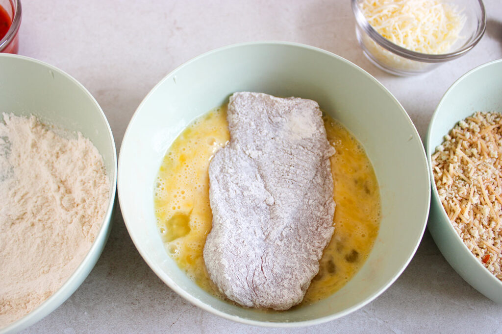 A floured chicken brest resting in egg wash.