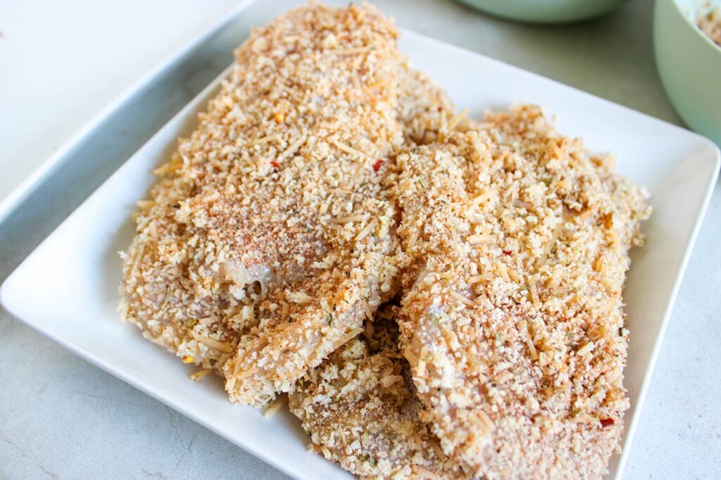 Breaded chicken breasts on a white platter.