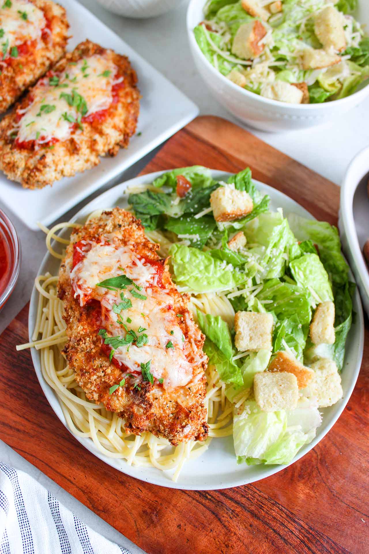Overhead focus of a plate holding a breast of Air Fryer Chicken Parmesan on a bed of spaghetti noodles with a side of green salad.