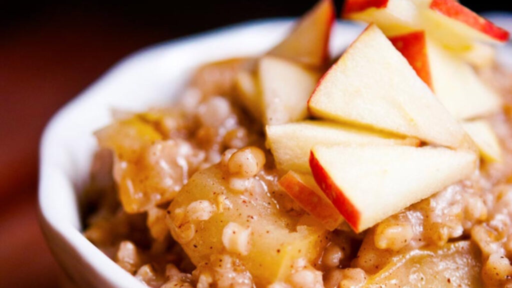 A closeup of a white bowl filled with apple pie oatmeal, topped with chopped pieces of apples.
