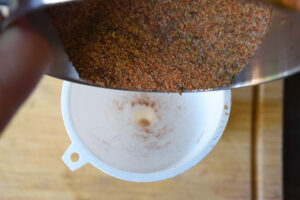 Pouring blackening seasoning through a funnel into a spice jar.