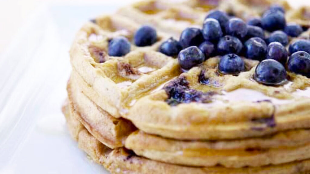 Closeup of a stack of blueberry waffles with fresh blueberries on top.