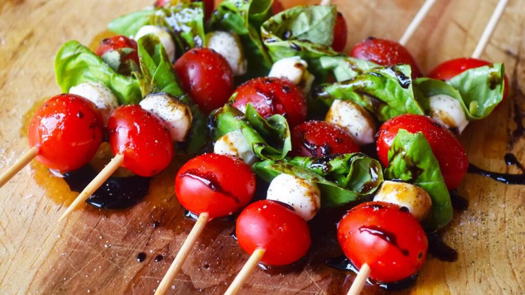 A line of Caprese Skewers on a wood surface drizzled with balsamic glaze.