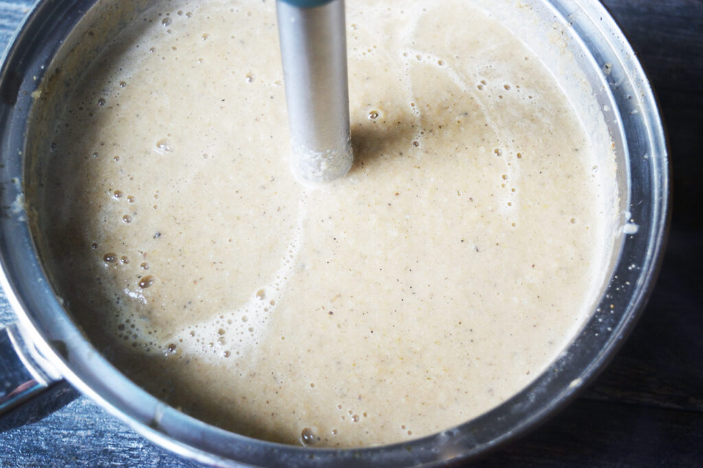 A stick blender in a pot of cauliflower soup.