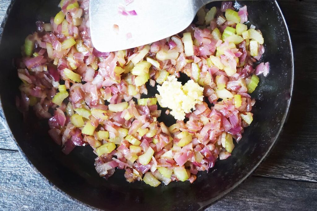 Garlic added to a skillet of saut&eacute;ing veggies.