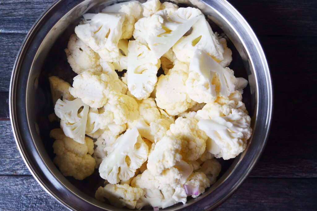 Raw cauliflower florets added to a pot of veggies.