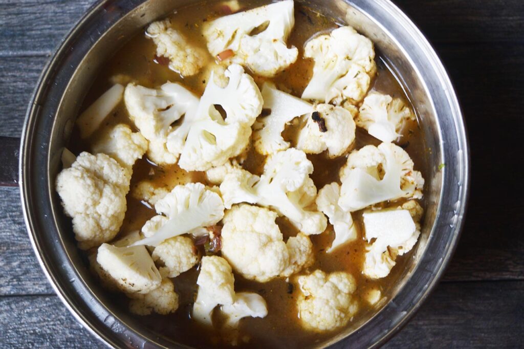 Broth added to cauliflower and veggies in a pot.