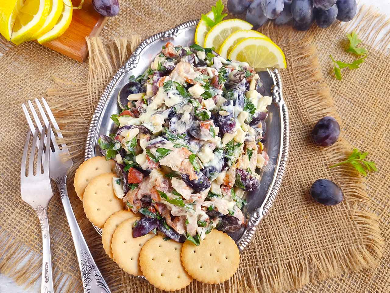 Overhead view of a silver platter filled with Chicken Salad With Grapes and a side of crackers.