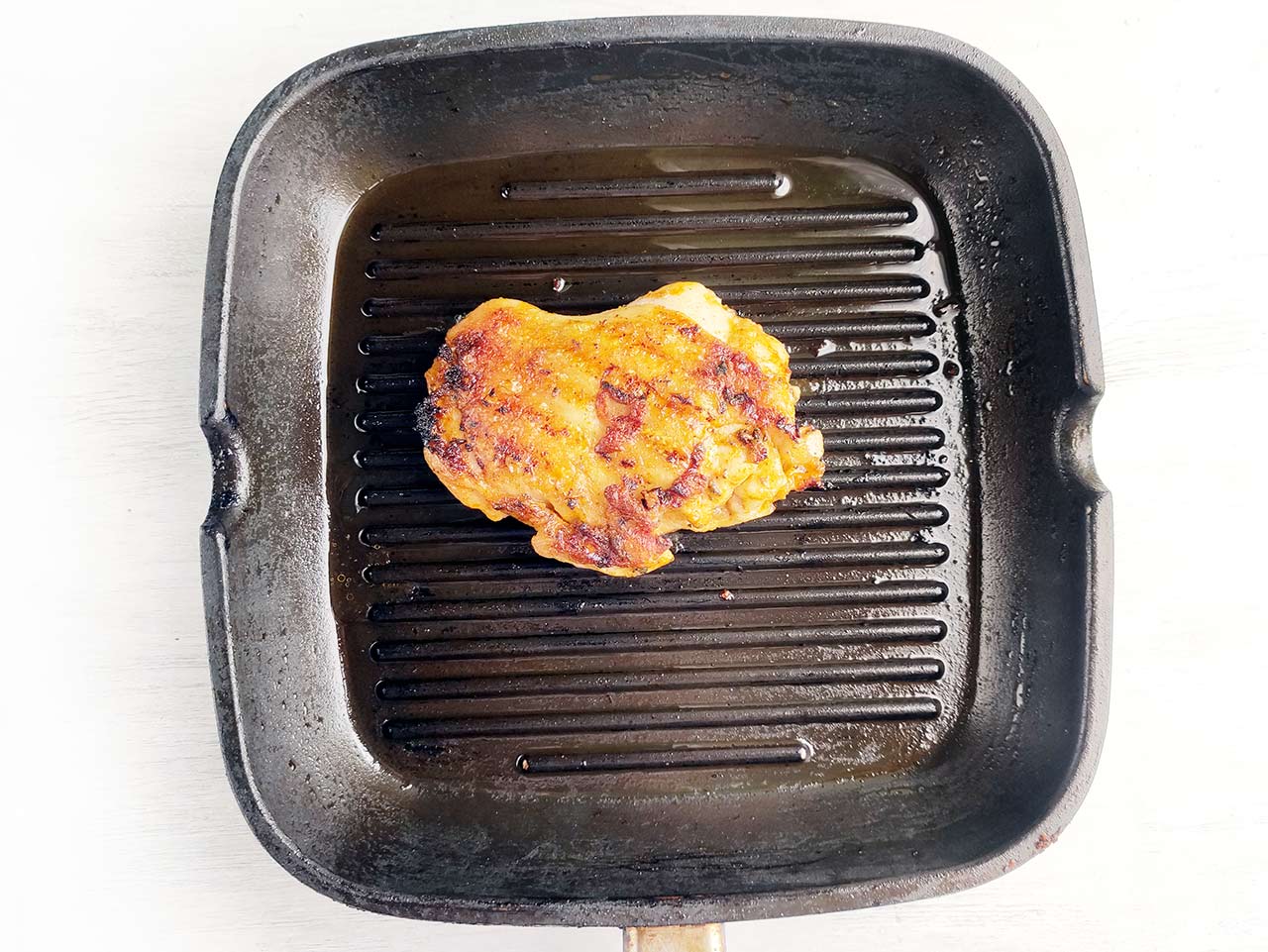 A chicken thigh cooked and sitting in a skillet.