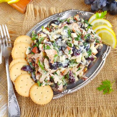 A silver platter with chicken salad on it with a side of crackers and lemon slices.