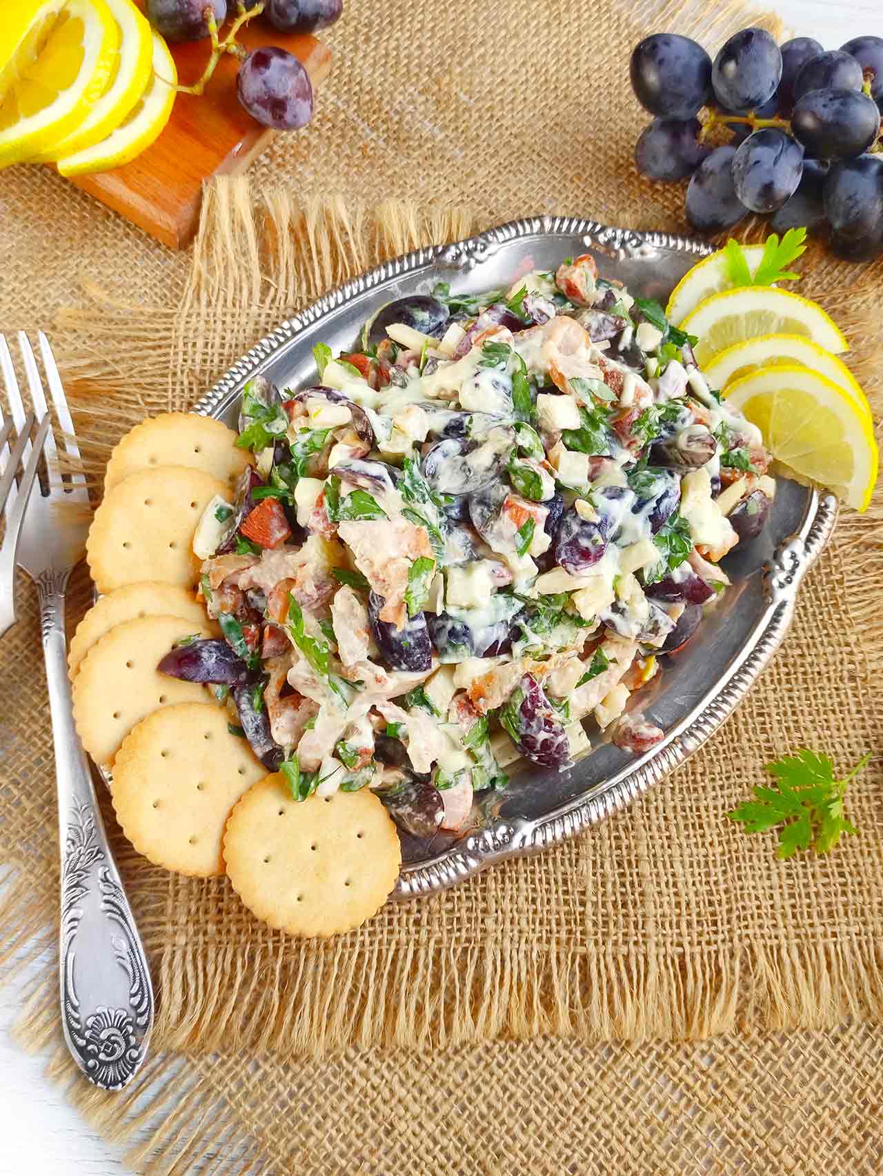 A silver platter with chicken salad on it with a side of crackers and lemon slices.
