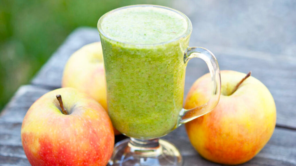 Side view of a glass mug full of Cinnamon Apple Smoothie, surrounded by three whole apples.