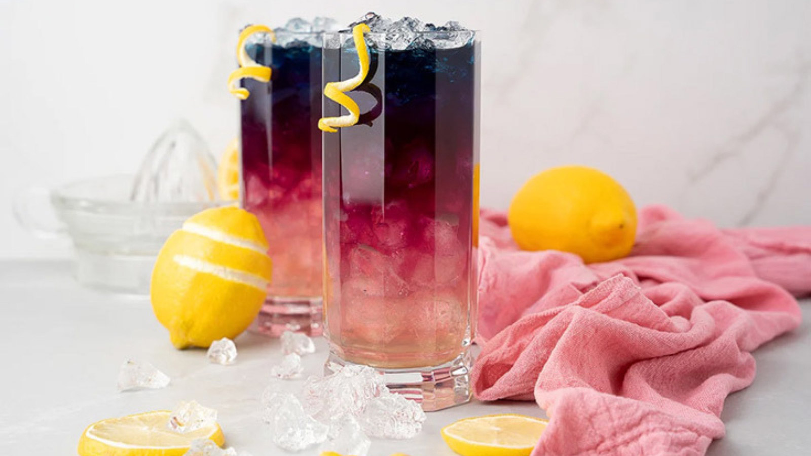 Two glasses of color-changing lemonade on a white surface and background.