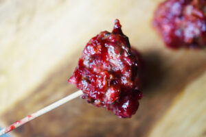 A wood skewer holds up a single Cranberry Glazed Turkey Meatball.
