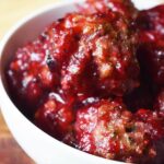 Closeup focus of a white bowl filled with Cranberry Glazed Turkey Meatballs.