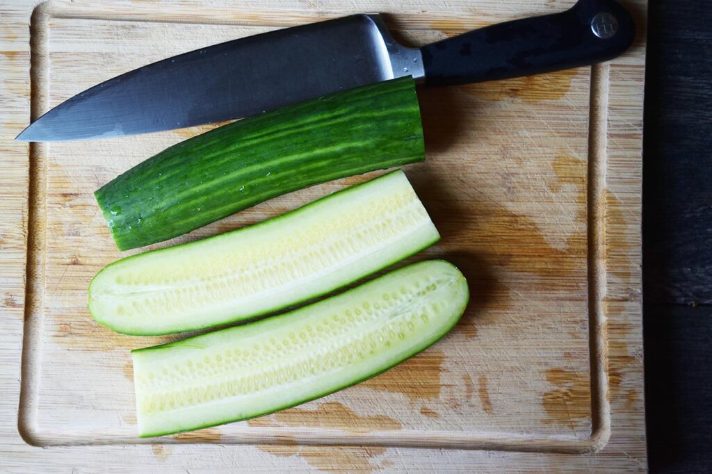 A partially cut cucumber laying on a cutting board.