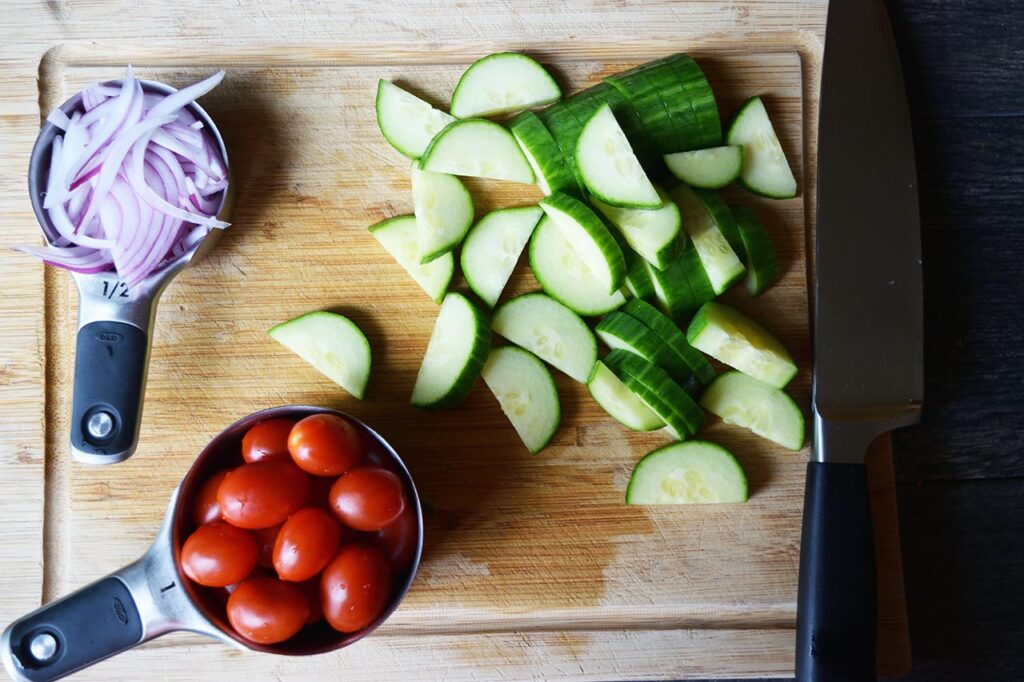 Cucumber salad vegetables cut and sitting on a wood cutting board.